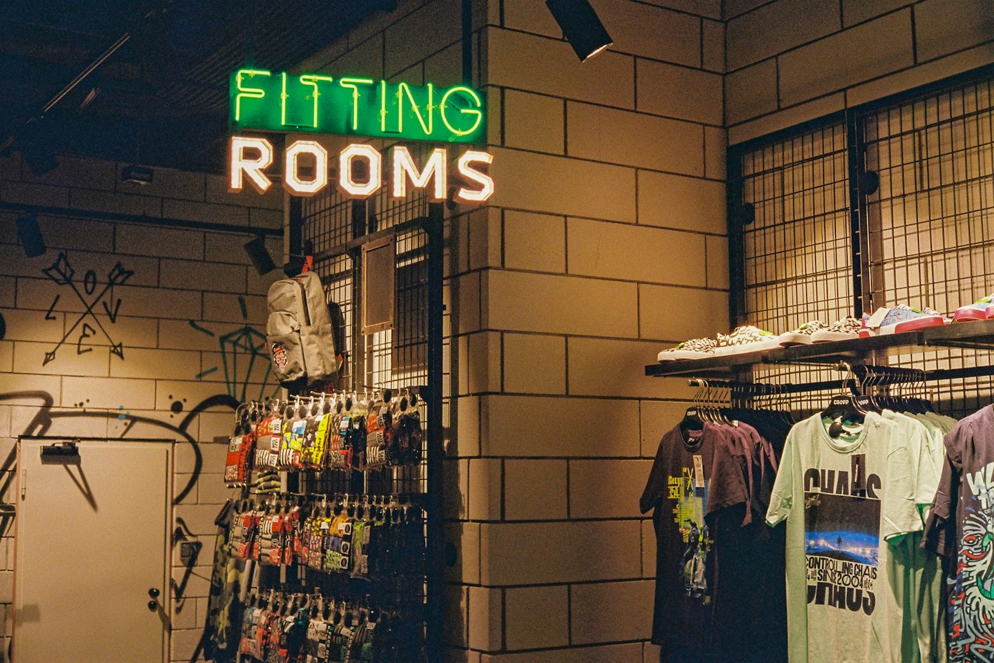 Green neon fitting rooms sign on a brick wall in a clothing store.