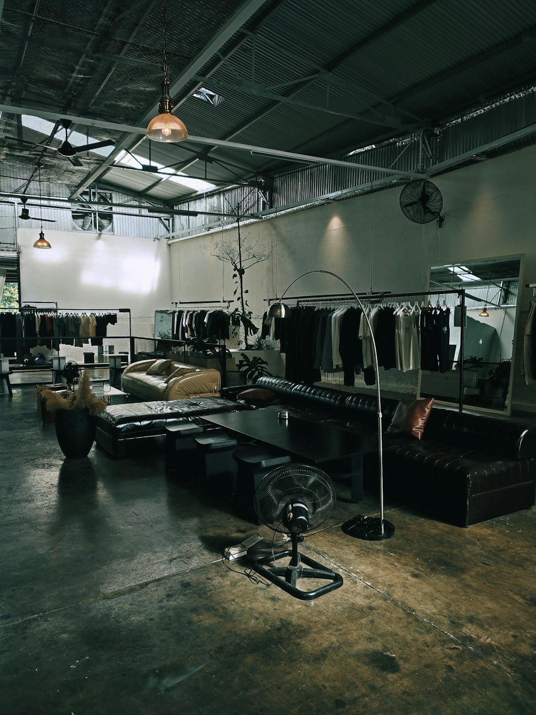 Contemporary clothing boutique with racks and leather seating on concrete floors.