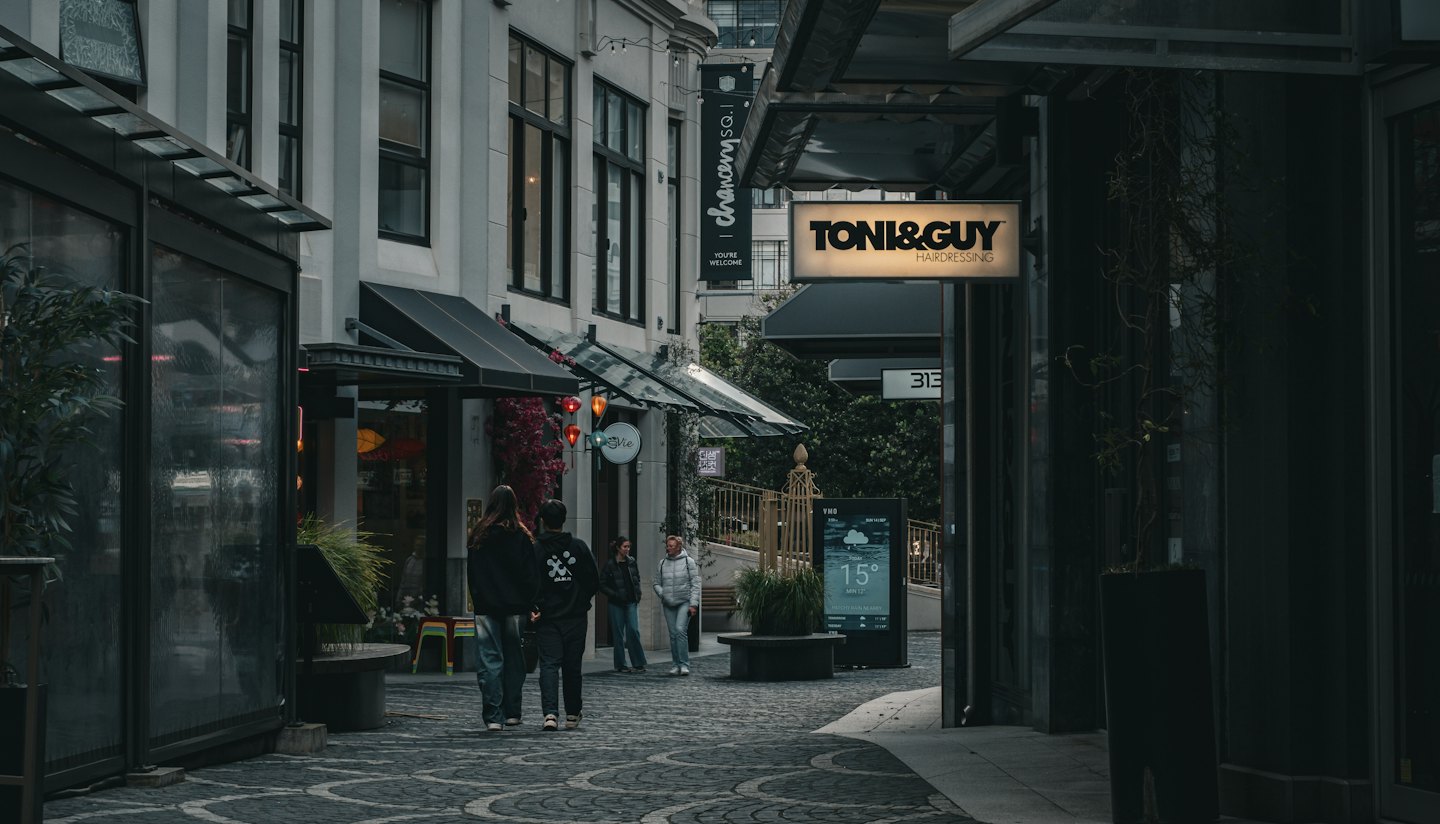 People walk through a modern city alley lined with shops.