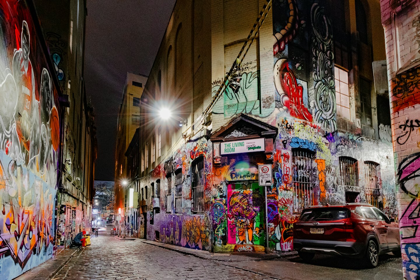 Graffiti covered alleyway with a red SUV and person walking.